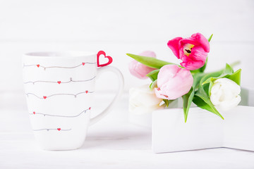 Colored tulips and cup with hearts on a white background