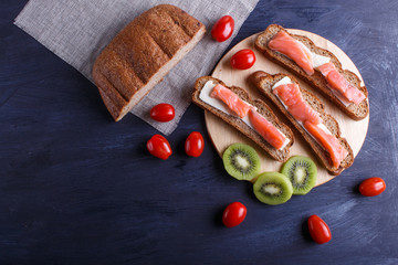 Smoked salmon sandwiches with butter on dark wooden background.