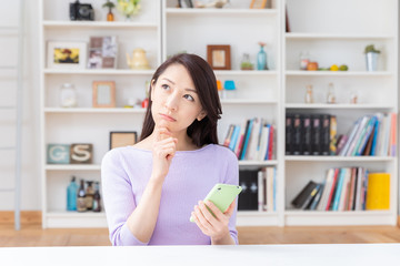 部屋でスマホを見る女性　考える