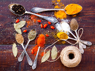 colorful spices in silver spoons on wooden table - pepper, curry, turmeric, paprika, sea salt, cumin, coriander
