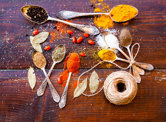 colorful spices in silver spoons on wooden table - pepper, curry, turmeric, paprika, sea salt, cumin, coriander