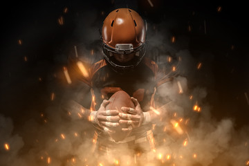 American football player on dark background in smoke and sparks in black and orange outfit. - 248556084