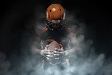 Fotobehang American football player on a dark background in smoke in black and orange equipment. © bondarchik