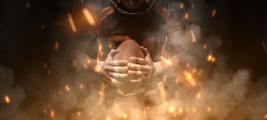 American football player on dark background in smoke and sparks in black and orange outfit.