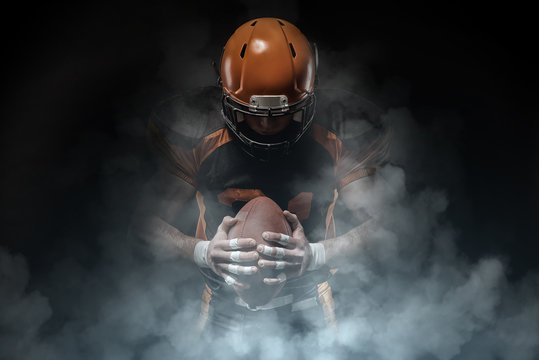 American football player on a dark background in smoke in black and orange equipment.