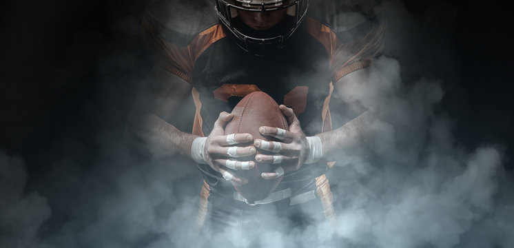 American football player on a dark background in smoke in black and orange equipment.