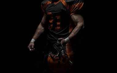 Fototapeta na wymiar American football player on a dark background in black and orange equipment.