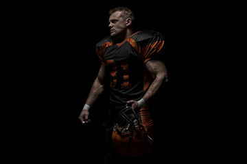 American football player on a dark background in black and orange equipment.