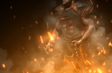 American football player on dark background in smoke and sparks in black and orange outfit.