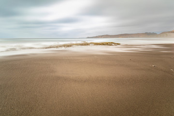 Amazing Las Brisas beach an awe sea coastline landscape on a wild environment in Chile. The sun goes down over the infinite horizon while the water stream push by the waves onto the algae and rocks