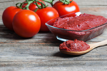 Tomato Paste in wooden spoon and ripe fresh grape tomatoes on wooden background. Cherry tomatoes. Tomato sauce ketchup food concept