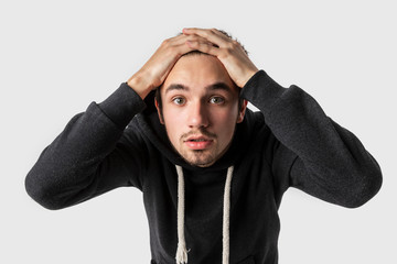 Frightened caucasian young man is looking into the camera with hands on his head. Mistake concept.