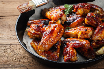 Baked chicken wings in barbecue sauce in a cast iron pan on an old wooden rustic table © Vasiliy