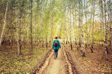 Girl with a backpack walks through the autumn forest