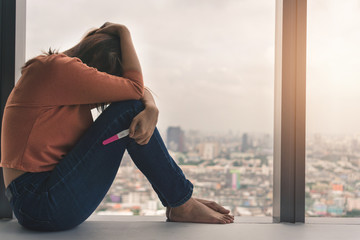 Unhappy young asian woman holding pregnancy test showing a negative result and sit down near big...