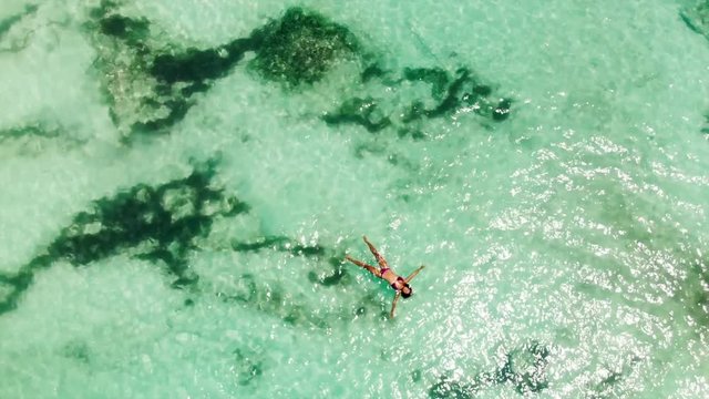 Aerial: Beautiful Young Woman in Bikini Floating in Crystal Clear Ocean
