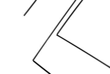 Black straws lay geometrical on a white background. Straws is a small plastic or paper pipe that allows its user to more conveniently consume a beverage like  water, tea, soda,cocktails,coffee, juice.