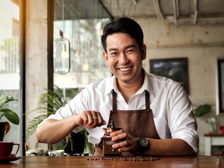Happy Asian barista man grinding coffee beans on table, lifestle concept.