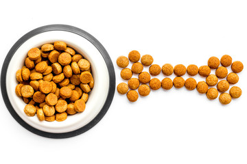 Dog food. Dry food in shape of bone near bowl on white backgorund top view space for text