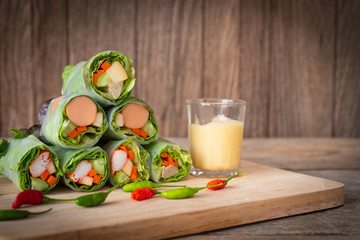 Salad rolls placed on a wooden table with chilli placed in front of and salad dressing placed beside.