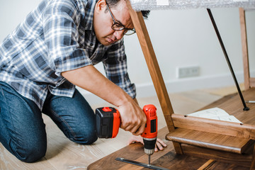 Fototapeta premium Man using hand drill to assemble a wooden table
