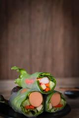 Salad rolls on black plate placed on a wooden table with chopsticks placed backside.