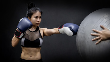 Plakat Young Asian girl boxer in sportswear punching exercise ball with blue boxing gloves in fitness gym. Martial arts training concept