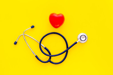 Heart health, health care concept. Stethoscope near rubber heart on yellow background top view copy space