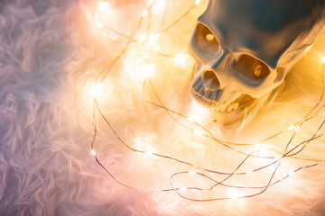 Fototapeta na wymiar Human skull on white fur carpet with decorative Christmas lights. Studio shot for Halloween festival holiday concept
