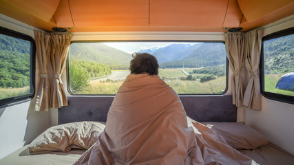 Young Asian man traveler staying in the blanket looking at mountain scenery through the window in...