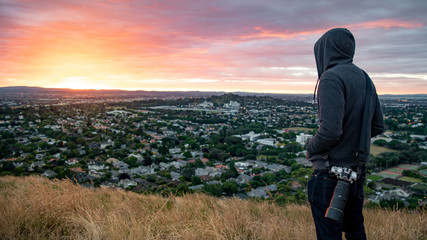 Fototapeta premium Hoodie man photographer and traveler watching sunrise over Auckland city at Mount Eden view point in Auckland, North Island, New Zealand. Travel Oceania. Success or achievement concepts