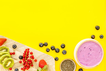 Preparing healthy fruit smoothie. Acai smoothie bowl near cutting board with fresh fruits, berries, chia seeds on yellow background top view space for text