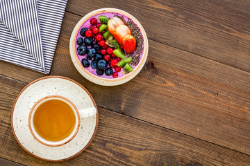 Light breakfast or healthy snack. Acai smoothie bowl with fresh fruits, berries, chia seeds on dark wooden background top view space for text