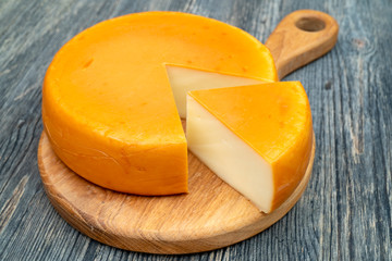 Fresh, round cheese on cutting board. Sliced piece.