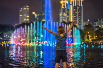 Boy on background of colorful fountain on the lake at night, near by Twin Towers with city on...