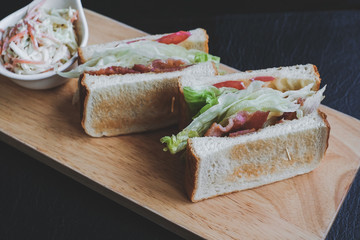 Appetizing sandwich on a wooden board with filling from lettuce, slices of fried bacon and tomato