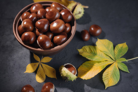 Chestnuts castanas in clay bowl on black background.