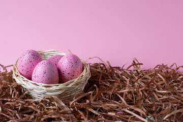Four pink Easter eggs in a basket on pink background. Easter celebratory wallpaper with copy space.