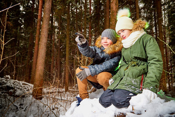 Children boy and girl sitting in snow forest in a winter day. Teenagers having trip and rest in weekend outdoor