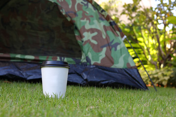 hot coffee drink, white disposable cup on green grass lawn campsite