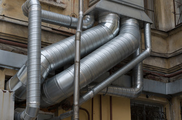 Interlacing of silver air ducts of different diameters on the old building closeup