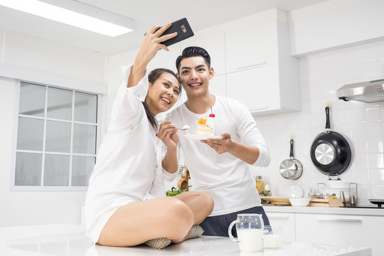 Young couple eating cake and take a picture together in kitchen at home