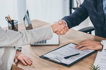 cropped view of shaking hands businessman and woman over table in office, compensation concept