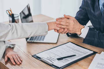 cropped view of businessman holding woman hand over table in office, compensation concept