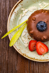 Chocolate dessert on a plate with pistachios, strawberries and blueberries on a wooden table, top veiw