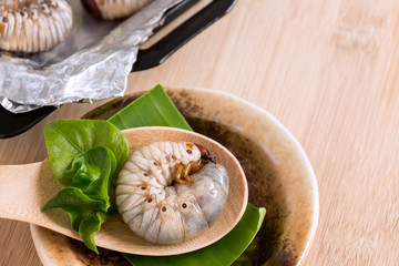 Grub Worms or Coconut Rhinoceros Beetle. Insects food for eating larvae fried or baked in spoon with vegetable on plate and on baking tray is good source of protein which edible. Entomophagy concept.