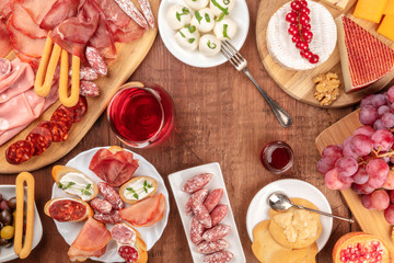 Charcuterie Tasting. A photo of many different sausages and hams, cold cuts, and a cheese platter, shot from the top on a rustic background with a glass of red wine, grapes and copy space