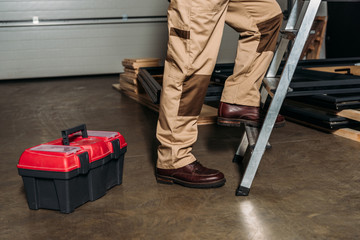 cropped view of repairman in orange uniform climbing on ladder in garage