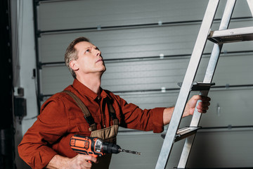 repairman climbing with screwdriver on ladder in garage