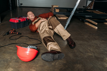 repairman lying on floor in uniform near ladder and holding on side in garage